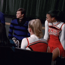 a cheerleader wearing a vmhs uniform sits in a classroom
