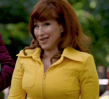 a woman with red hair and a yellow jacket is smiling