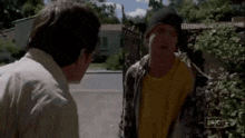 a man in a yellow shirt is talking to another man in a black hat ..