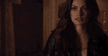 a woman in a leather jacket is standing in a dark room looking at the camera .