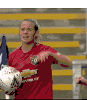 a woman in a red shirt is holding a soccer ball and pointing at the camera .