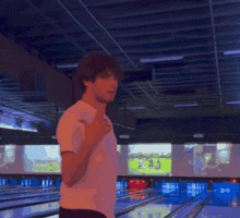 a man in a white shirt is standing in a bowling alley giving the middle finger