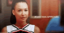 a cheerleader is standing in front of a red wall and a sign that says santana approves