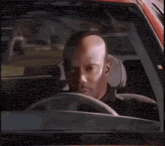 a bald man is sitting in the driver 's seat of a car looking at the camera .