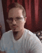 a man with glasses and a beard is wearing a white shirt and a chain around his neck .