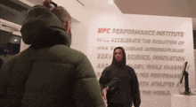 a man in a hooded jacket stands in front of a wall that says ufc performance institute