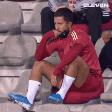 a man wearing a red adidas shirt sits on a bleacher