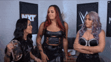 three women are standing in front of a wall that has nxt written on it