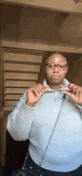 a woman wearing glasses and a light blue sweater is standing in front of stairs .