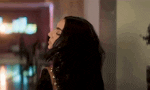 a woman with long black hair is standing in a dark room with her eyes closed and her hair blowing in the wind .