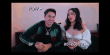 a man and a woman are sitting next to each other on a bed with a play button above them