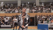 a man in a leather jacket is standing in front of a crowd of people in a stadium .