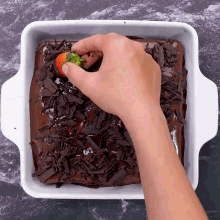 a person is putting a strawberry on top of a chocolate covered cake