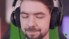 a man with a beard is wearing headphones with his eyes closed and a green background .