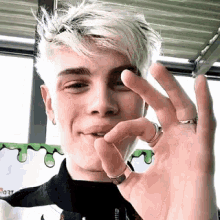 a young man with a ring on his finger is making a peace sign with his hand .