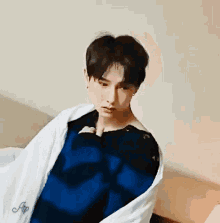 a young man is sitting on a bed wrapped in a blanket and looking at the camera .