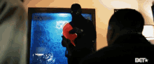 a man in a black mask is standing in front of a stained glass door with a bet logo on the bottom