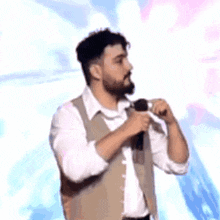 a man with a beard is holding a microphone in his hand and singing into it .