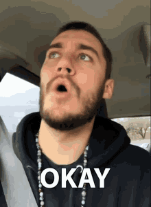 a man with a beard is wearing a black hoodie and a necklace with the word okay on it