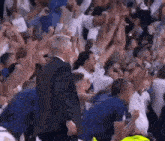 a man in a suit is walking through a crowd of people at a basketball game .