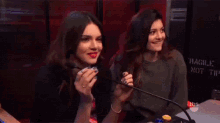 two women are standing next to each other in front of a microphone and making funny faces .