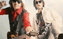 two men are standing next to each other playing guitars .