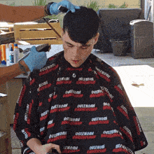 a man is getting his hair cut by a barber wearing a cape that says dale noah barbershop