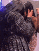 two women are hugging each other and one is covering her face with her hands .