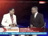 two men are sitting in front of a sign that says ' live morning breeze ' on it