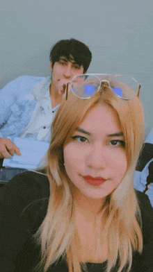 a woman wearing sunglasses takes a selfie with a man in the background