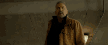 a man with a beard wearing a brown jacket looks up