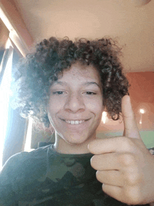 a young boy with curly hair giving a thumbs up