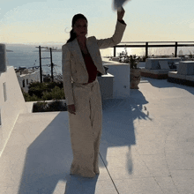 a woman in a white suit is standing on a balcony with her hand up