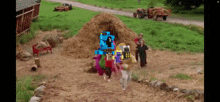 a group of people are standing in a field with a pile of hay in the background .