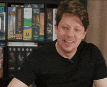 a man in a black shirt is smiling in front of a shelf full of games