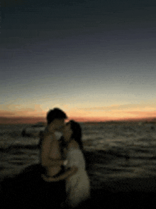 a blurry photo of a man and woman kissing on the beach at sunset .