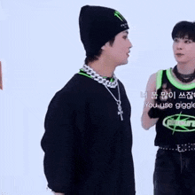 a man wearing a black beanie and a necklace is standing next to another man wearing a green tank top .