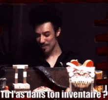a man is sitting at a table with food and the words " tu l'as dans ton inventaire "