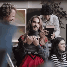 a man with long hair and a beard is holding a book in front of a group of people including a woman