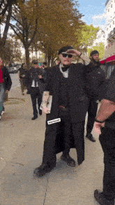a man in a black coat and hat is walking down a sidewalk with a group of people .