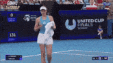 a woman walking on a tennis court with a united cup finals sign in the background