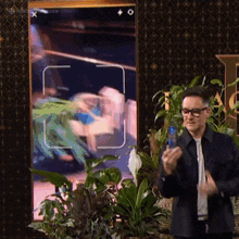 a man wearing glasses is holding a cell phone in front of a screen that says ' word of the day ' on it