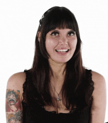 a woman with a tattoo on her arm is wearing a black tank top and smiling .