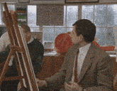 a man in a suit and tie is looking at a painting on an easel in front of a window