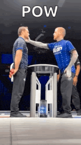 two men are standing next to each other in front of a table and one of them is giving the other a slap on the face .