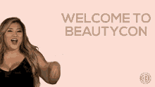 a woman is flexing her muscles in front of a pink background that says `` welcome to beautycon '' .
