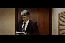 a man in a suit and tie is standing in front of a door holding a tablet computer .