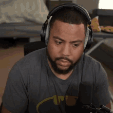 a man with a beard is wearing headphones and a batman shirt while sitting in front of a microphone .