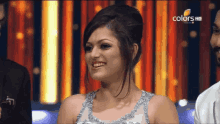 a woman in a silver dress is smiling in front of a curtain that says colors hd