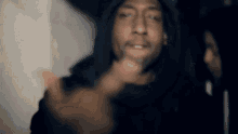 a man in a hooded jacket is pointing at the camera while a woman looks on .